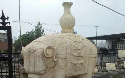 这是一尊位于别墅小区的大象雕塑，它背负着一个花瓶，…
